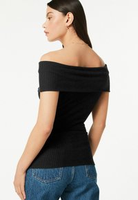 Melna off-shoulder ribota blūze ar pieguļošu fasonu un teksturētu audumu, apvienota ar augsto vidukli džinsu biksēm. Uzsvars uz dekoltē un tekstūru.
