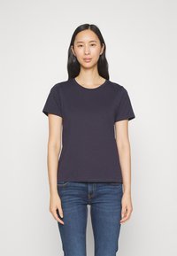 Granatowa koszulka typu crew-neck wykonana z bawełny, z krótkim rękawem, zaprezentowana na modelu w dopasowanych dżinsach na jednolitym jasnym tle.