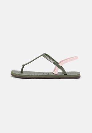 Zielona gumowa klapka ze różowym paskiem, teksturowaną wkładką i brązową podeszwą. Posiada logo "Havaianas" na pasku.