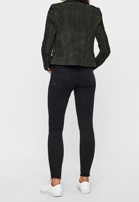 Černá semišová bunda s přiléhavým střihem, spárovaná s černými skinny džíny s třepícím se lemem a bílými teniskami.