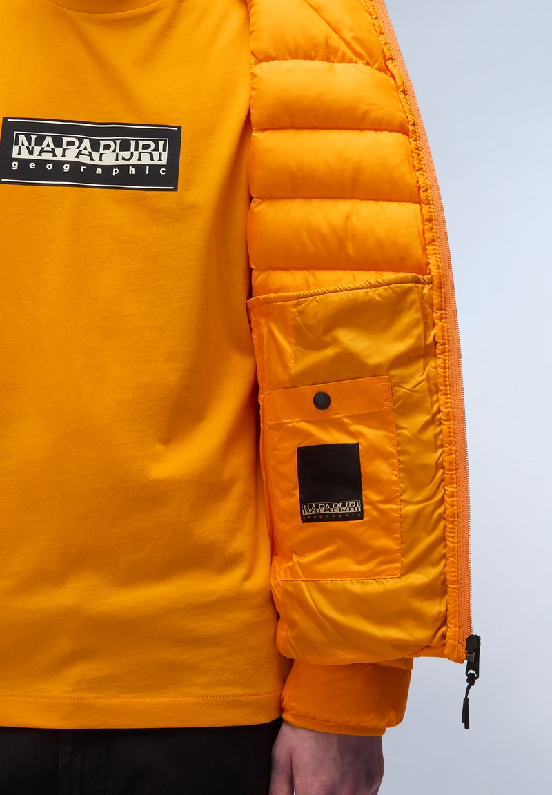 Chaleco inflable naranja con cremallera, que presenta secciones acolchadas y un bolsillo con solapa. Lleva puesto un camiseta naranja a juego con un logo.