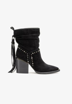 Czarny zamszowy botek za kostkę o luźnym fasonie, ozdobiony metalowymi ćwiekami i elementami, z masywnym, teksturowanym obcasem oraz detalem z frędzlami.