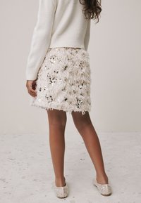 Puhasta, do koljena duga suknja u blijedo ružičastoj boji s višeslojnim resama i raspršenim šljokicama. Uparena s mekanim, svijetlim cipelama bez vezica.