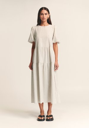 Light gray striped midi dress with short puff sleeves, tiered design, round neckline, made of textured fabric, paired with black sandals.