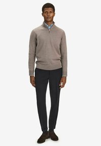 Beige neulepullover, jossa on puoliveto-kaulus, yhdistettynä muototuotettuihin mustiin housuihin ja ruskeisiin kenkiin. Tyylikäs, minimalistinen muotoilu, jossa on ribbireunukset.
