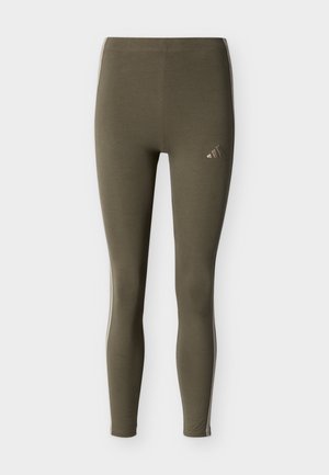 Leggings femme vert olive avec des bandes blanches sur les côtés et un petit logo Adidas réfléchissant sur la cuisse supérieure.