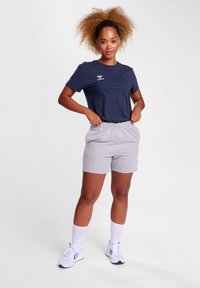 Marine T-skjorte med logo, grå shorts, hvite ankelstrømper og joggesko. Antrekket har en avslappet passform og myk tekstur.