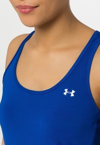 Top atletico blu in tessuto liscio e elastico; presenta un colletto rotondo e un logo bianco sul lato superiore sinistro.
