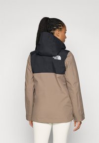 Smeđa i crna vodootporna jakna s kapuljačom, koja se odlikuje kontrastnim blok dizajnom i logotipom The North Face na gornjem dijelu leđa.