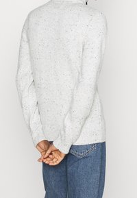 Maglione grigio chiaro con un tessuto a maglia testurizzato, caratterizzato da un collo rotondo e polsini a costine, abbinato a jeans in denim blu.