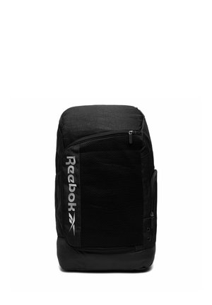 Mochila negra Reebok con un gran bolsillo frontal de malla, logo vertical, cierres de cremallera y orificios de ventilación laterales sobre un fondo blanco.