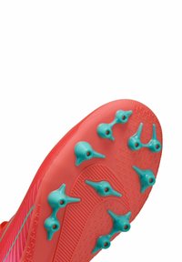 Suela de zapatilla de fútbol roja con tacos en color teal. Superficie con textura de agarre y diseño aerodinámico con sutiles acentos en rosa en los laterales.