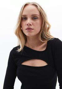 Schwarzes Langarm-Oberteil aus elastischem Material, mit einem runden Ausschnitt und einem zentralen Cut-Out-Detail unterhalb des Kragens.