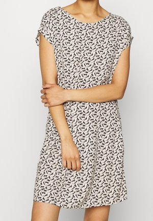 Vrouw draagt een kort mouw, knie-lange jurk met een zwarte kattenprint op een lichte achtergrond, met gekruiste armen ter hoogte van de taille.