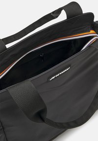 Black duffel bag with nylon material, featuring robust webbed handles, a zippered closure, and a contrasting inner pocket with orange accents.