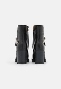 Zwarte leren enkellaarsjes met een afgeronde neus, hoge blockhakken en ritssluitingen aan de achterkant. Voorzien van goudkleurige hardware accenten.