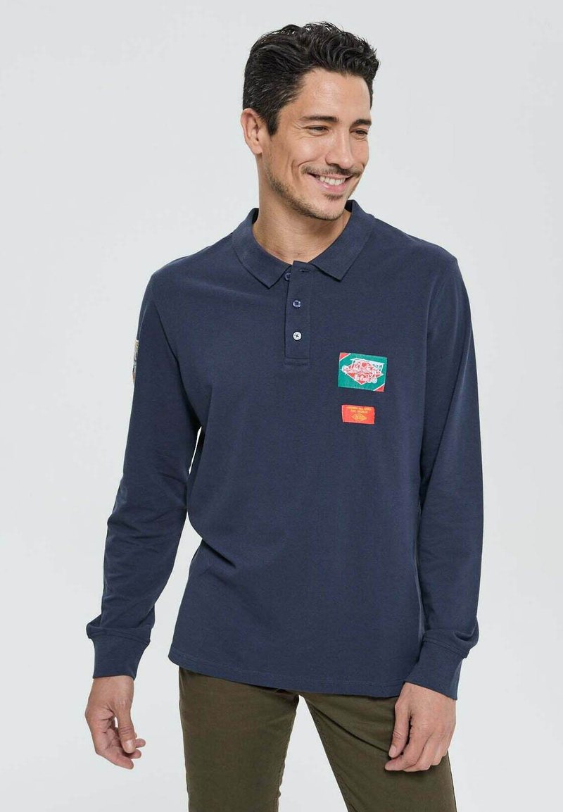 Polo à manches longues bleu marine en coton, avec un col, deux poches sur la poitrine en vert et rouge, et une coupe décontractée.