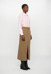 Camicia rosa con bottoni e fiori ricamati, abbinata a una gonna marrone al ginocchio con spacco frontale e tasche a pattina. Stivali neri con tacco.