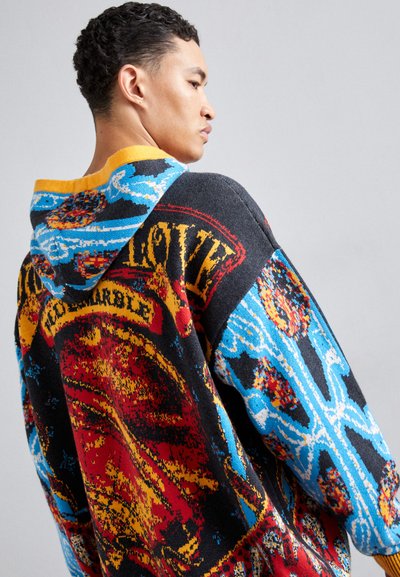 Knit hoodie featuring multicolored patterns in red, blue, and yellow, with a large front graphic and contrasting hood. Soft texture, relaxed fit.