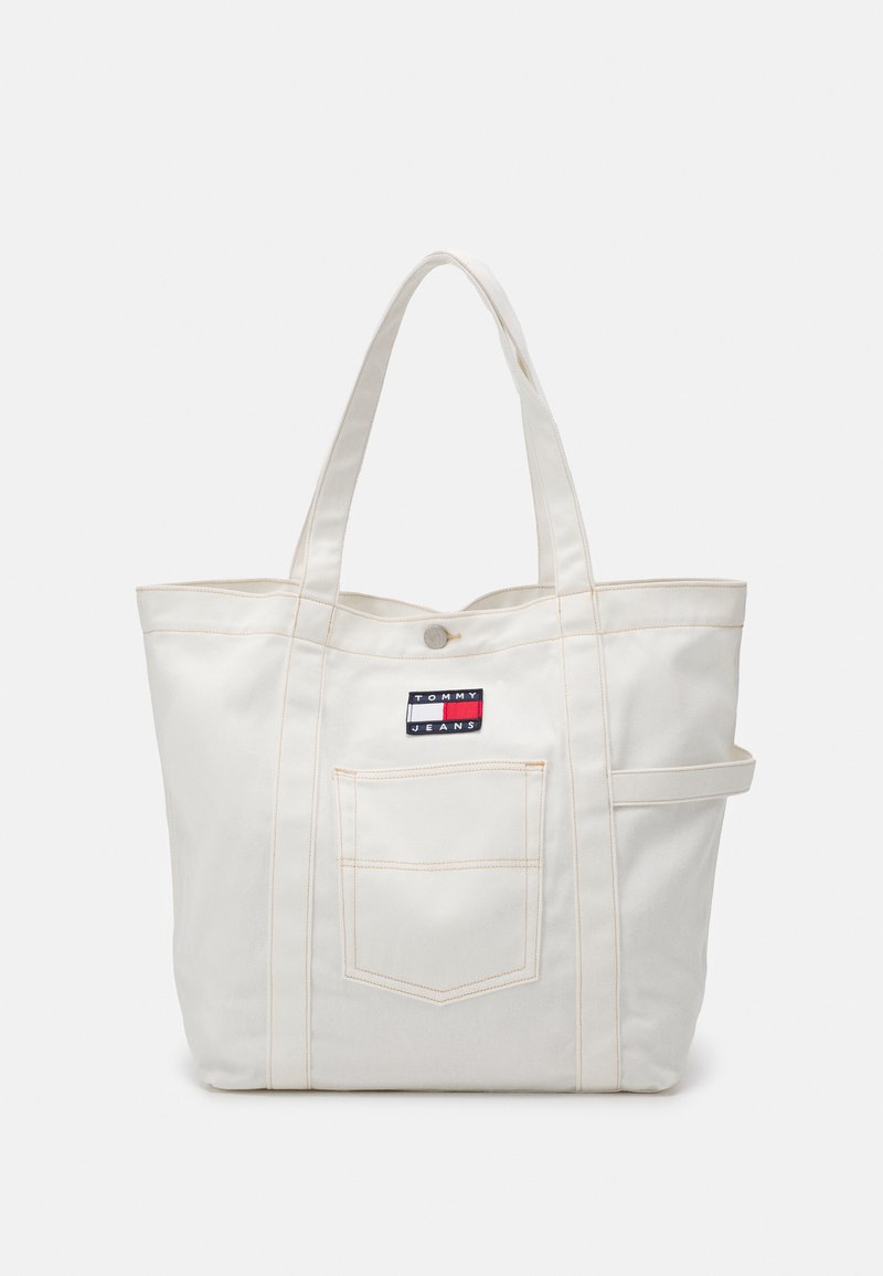 Oficialus tote krepšys iš drobės, off-white spalvos, su kontrastingomis siūlėmis, turintis priekinį kišenę ir Tommy Jeans logotipo etiketę. Dvi tvirtos petnešos.