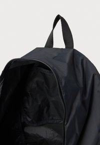 Zaino leggero nero con chiusura a zip. Presenta una superficie testurizzata, un design semplice e una maniglia superiore per un facile trasporto.