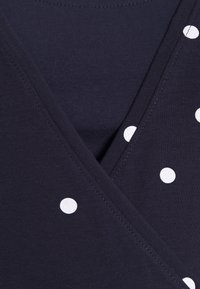 Námorně modrá tkanina s překrývajícím se výstřihem do V a rozptýlenými bílými puntíky na jedné straně.