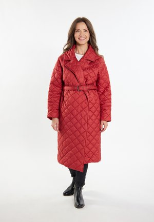 Cappotto lungo trapuntato rosso con vita cinfigurata, grande colletto e apertura frontale diagonale. Superficie testurizzata con motivo a diamante, indossato sopra jeans neri e stivali.