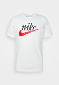 Valkoinen puuvillapaita, jossa on suuri musta "nike" -teksti ja punainen swoosh-logo. Pyöreä kaula-aukko ja lyhyet hihat. Normaali istuvuus.