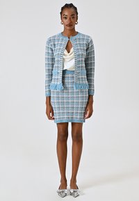 Cardigan a maglia a quadri blu con bordi sfrangiati e gonna coordinata, indossato su un top in satin crema; abbinato a ballerine metalliche con punta a punta.