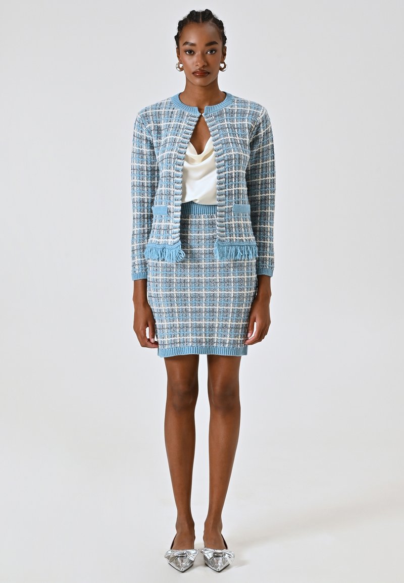 Cardigan a maglia a quadri blu con bordi sfrangiati e gonna coordinata, indossato su un top in satin crema; abbinato a ballerine metalliche con punta a punta.