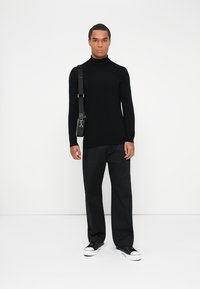 Czarny sweter z golfem i długimi rękawami, w połączeniu z czarnymi spodniami typu wide-leg oraz czarnymi sneakersami na sznurówki. Minimalistyczny design, gładka faktura.