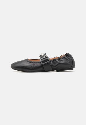 Chaussure plate en cuir noir avec bout arrondi, arrière élastiqué et bride décorative ornée d'une boucle rectangulaire et de petits clous argentés.