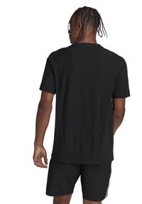 Maglietta sportiva nera a maniche corte con un tessuto strutturato, vestibilità comoda e un semplice colletto tondo. Indossata con pantaloni corti neri con strisce laterali.
