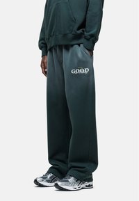 Groene joggingbroek met een verloop van donker naar licht, voorzien van een 'GOOD' tekstafbeelding op het linkerbeen en zijzakken.
