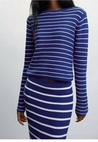 Femme portant un pull à manches longues rayé horizontalement bleu et blanc et une jupe assortie, visible du cou aux hanches.