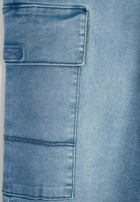 Jasnoniebieska tkanina dżinsowa z dużą, naszywaną kieszenią po boku, z widocznymi detalami stębnowania, fakturą i gładkim wykończeniem.