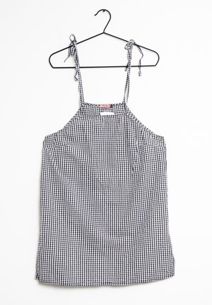 Vestido sin mangas con estampado de cuadros en blanco y negro y tirantes para atar, colgado en una percha negra sobre un fondo blanco.