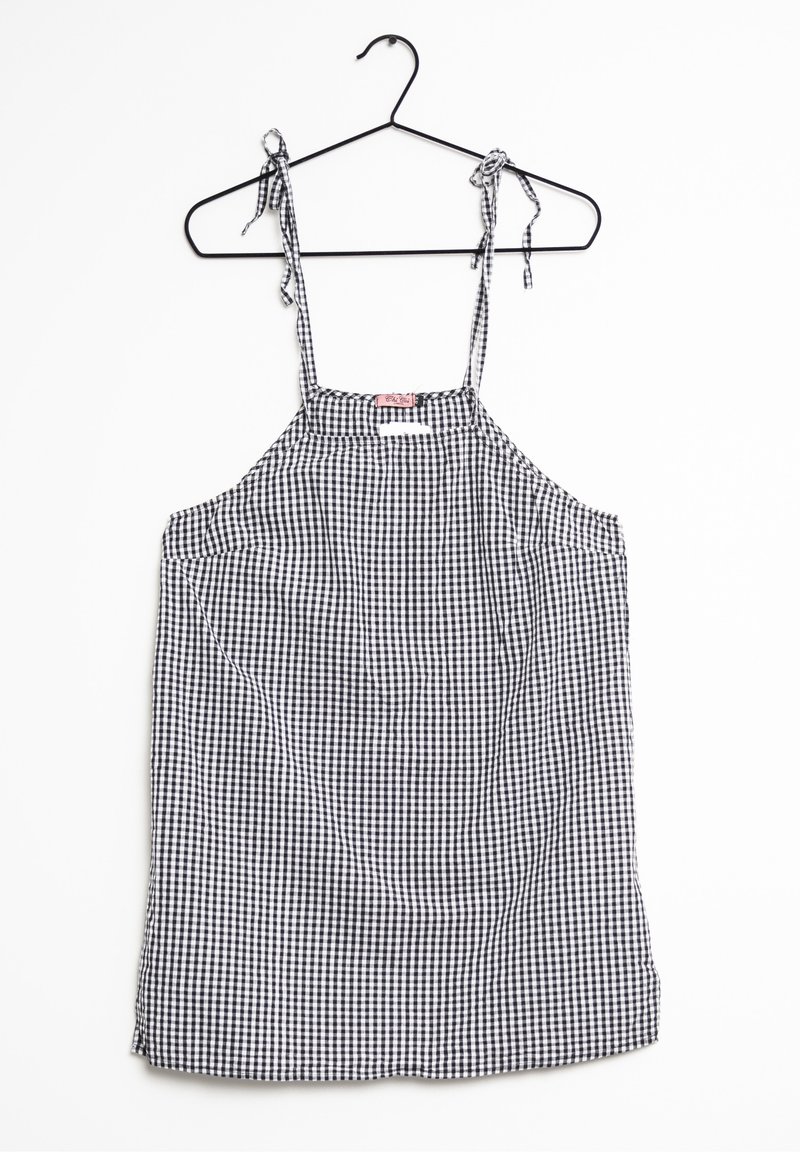 Robe sans manches à carreaux noir et blanc avec bretelles à nouer, suspendue à un cintre noir sur fond blanc.