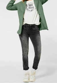 Zelený kardigan, bílé tričko s nápisem "time bloom" a černé úzké džíny. Outfit doplňují robustní bílé tenisky.