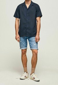 Navy lyhythihainen nappipaita, vaaleansiniset kuluneet denim-shortsit, kreeminväriset tennarit ja beigejä perussukat. Minimalistinen muotoilu ja pehmeä tekstuuri.