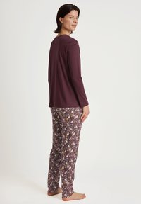 Langarmige bordeauxrode top, gecombineerd met pyjamabroek met een patroon van bloemen en dieren in schakeringen van paars, geel en wit.