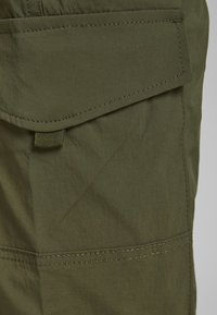 Olivgrön cargobyxa med raka kanter och synliga sömmar. Har ett vävt band för säker stängning. Slät tygtextur.