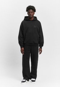 Black hoodie and matching sweatpants made of soft fabric; features a front pocket and a small logo on the chest. Sneakers with white accents.