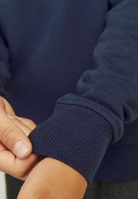 Navy blue sweatshirt featuring ribbed cuffs, soft texture, and a relaxed fit, with a hand adjusting the cuff visible.