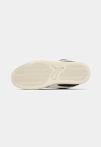 Black and cream sneaker sole with patterned traction, featuring a prominent logo silhouette and curved design for grip and comfort.