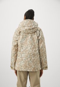 Beigefarbene gepolsterte Parka mit floralem Camouflage-Muster. Verfügt über eine geräumige Kapuze und verstellbare Bündchen. Glatte Textur und lockere Passform.