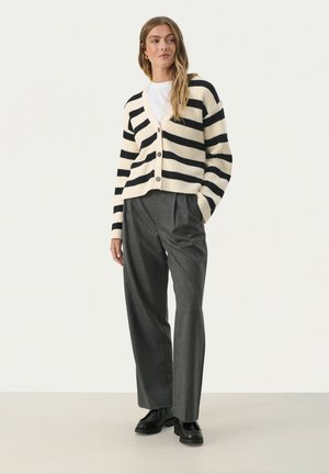 Striped cardigan in cream and black with a V-neckline and three buttons, paired with tailored gray trousers and chunky black shoes.