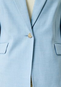 Světle modrý blazer z texturované tkaniny, s jedním knoflíkem, dvěma předními kapsami a přiléhavým střihem.