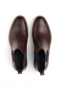 Brązowe skórzane botki za kostkę o gładkim wykończeniu, z elastycznymi panelami po bokach oraz ozdobnym szwem wokół podeszwy. Minimalistyczny design, bez widocznych oznaczeń marki.