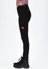 Black athletic pants with a fitted design, zippered pockets, and a patch. Paired with black hiking boots featuring textured soles.
